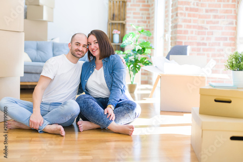 Young couple sitting on the floor arround cardboard boxes moving to a new house with a happy and cool smile on face. Lucky person.