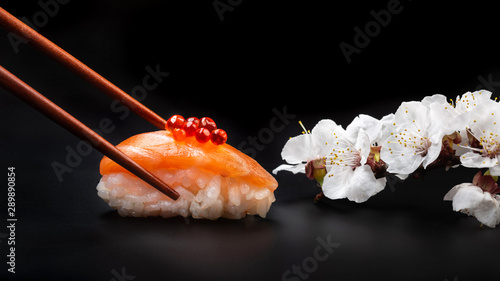Sushi with red caviar and white flowers on a black table. Macro