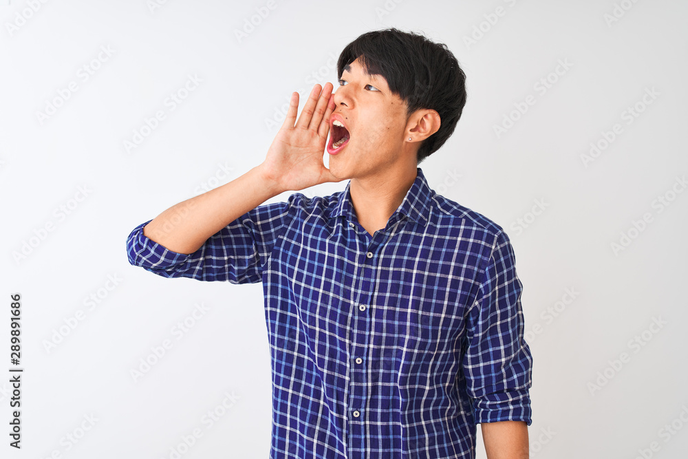 Young chinese man wearing casual blue shirt standing over isolated white background shouting and screaming loud to side with hand on mouth. Communication concept. Young chinese man wearing casual blue shirt standing over isolated white background shouting and screaming loud to side with hand on mouth. Communication concept.