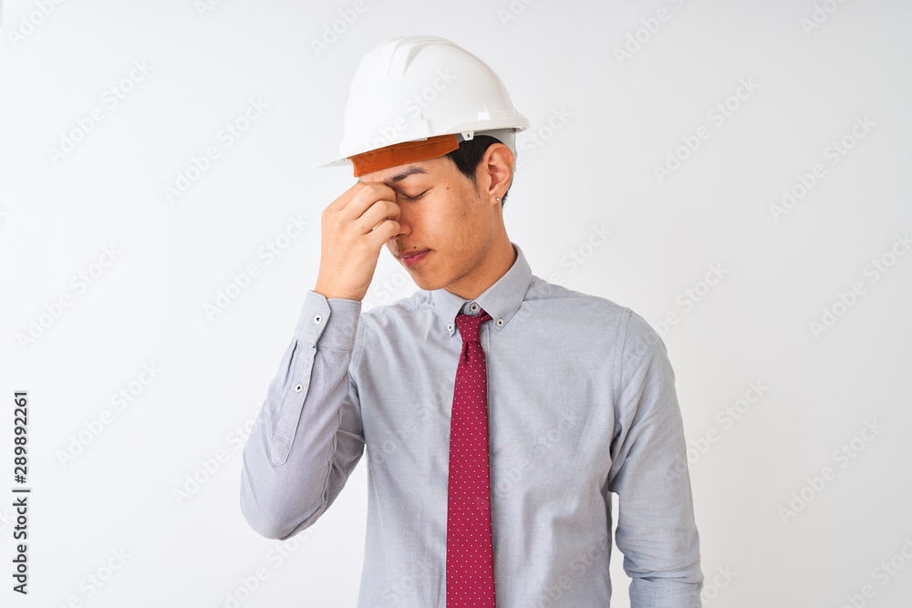Chinese architect man wearing tie and helmet standing over isolated white background tired rubbing nose and eyes feeling fatigue and headache. Stress and frustration concept. Chinese architect man wearing tie and helmet standing over isolated white background tired rubbing nose and eyes feeling fatigue and headache. Stress and frustration concept.