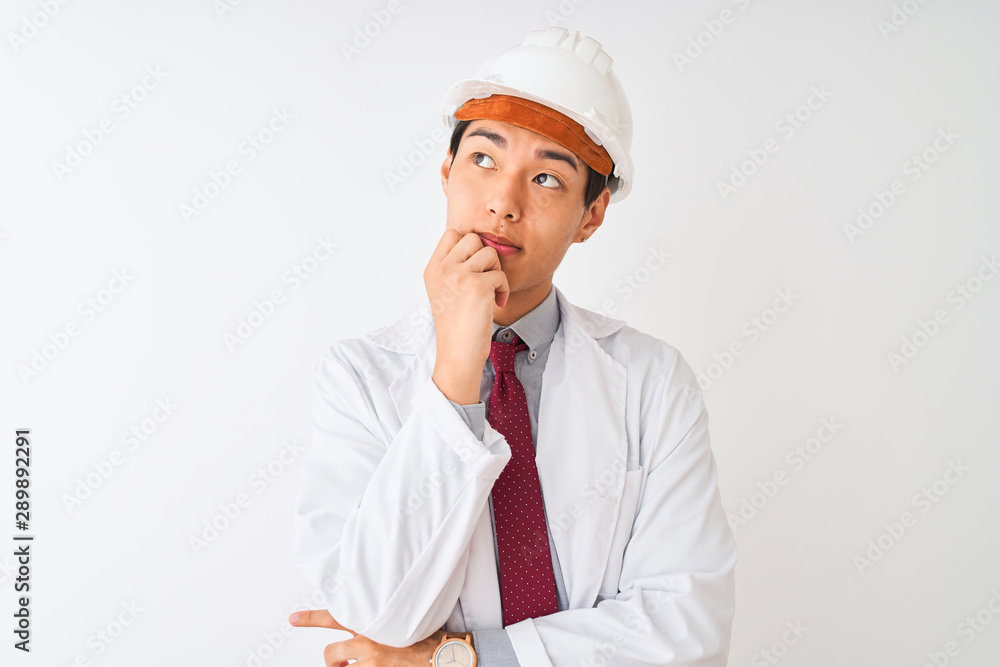 Chinese architect man wearing coat and helmet standing over isolated white background with hand on chin thinking about question, pensive expression. Smiling with thoughtful face. Doubt concept. Chinese architect man wearing coat and helmet standing over isolated white background with hand on chin thinking about question, pensive expression. Smiling with thoughtful face. Doubt concept.
