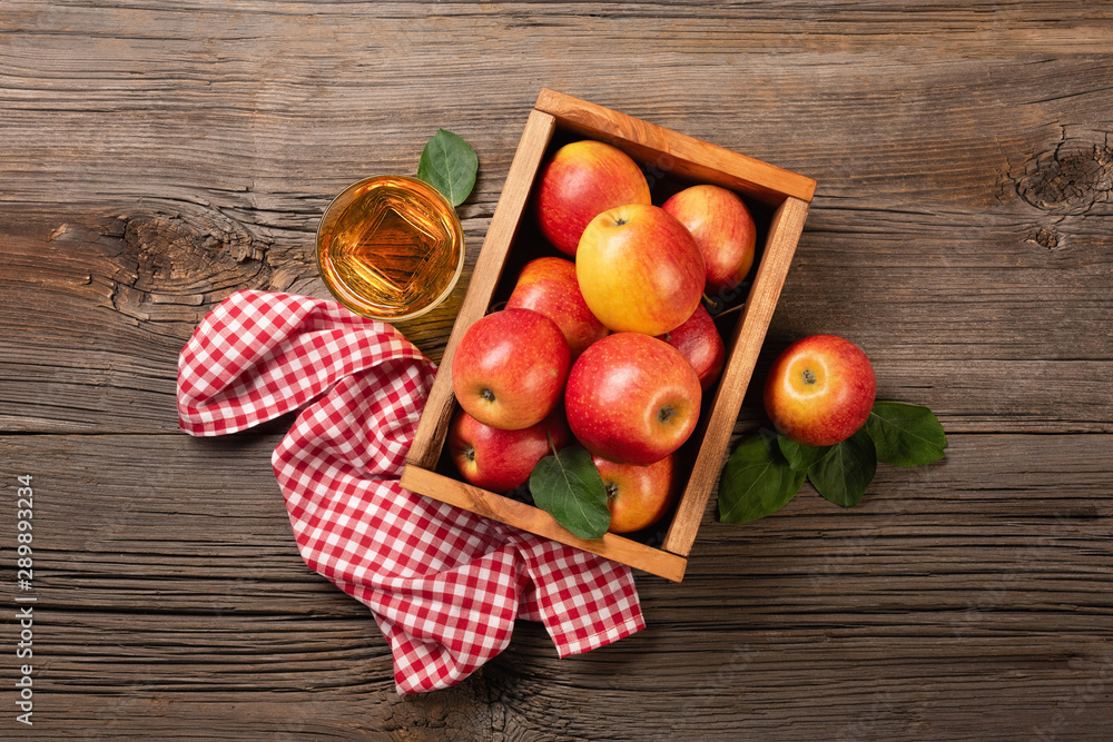 Ripe red apples in wooden box with branch of white flowers and glass of fresh juice on a wooden table Ripe red apples in wooden box with branch of white flowers and glass of fresh juice on a wooden table