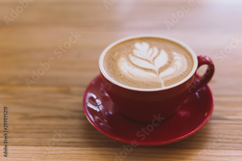 Cup of cappuccino with latte art on wooden background. Red ceramic cup.