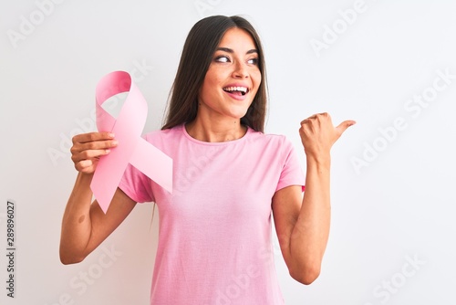 Young beautiful woman holding cancer ribbon standing over isolated white background pointing and showing with thumb up to the side with happy face smiling photo