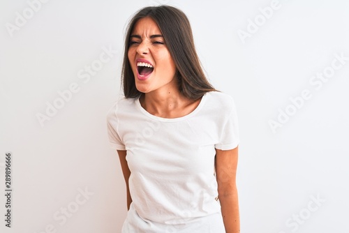 Young beautiful woman wearing casual t-shirt standing over isolated white background angry and mad screaming frustrated and furious, shouting with anger. Rage and aggressive concept. © Krakenimages.com