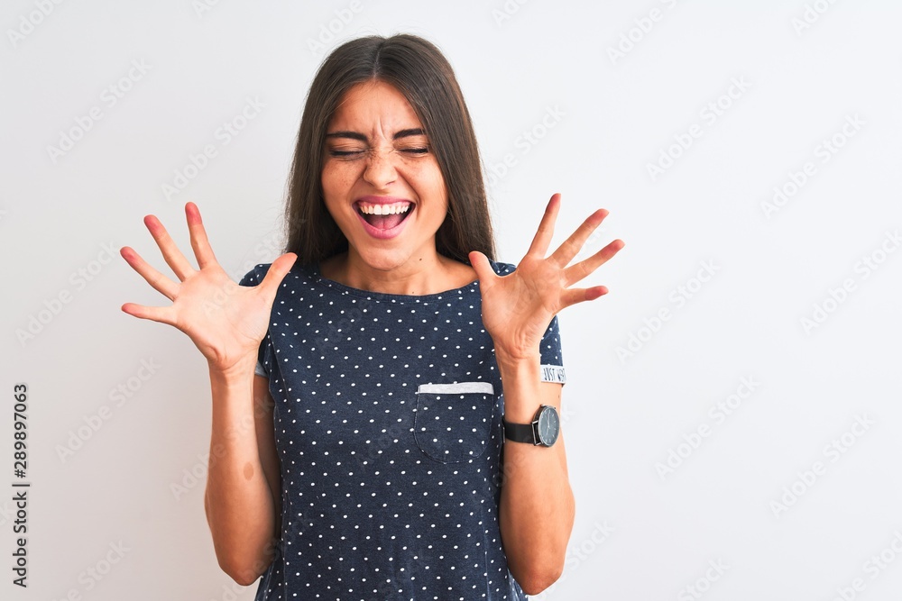 Young beautiful woman wearing blue casual t-shirt standing over isolated white background celebrating mad and crazy for success with arms raised and closed eyes screaming excited. Winner concept - obrazy, fototapety, plakaty 