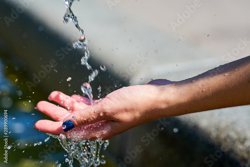                       Woman  s hand under a fresh stream of water in sunlight.         