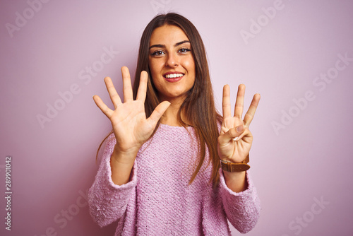 Young beautiful woman wearing casual sweater standing over isolated pink background showing and pointing up with fingers number eight while smiling confident and happy.