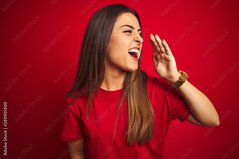 Young beautiful woman wearing t-shirt standing over isolated red background shouting and screaming loud to side with hand on mouth. Communication concept. Young beautiful woman wearing t-shirt standing over isolated red background shouting and screaming loud to side with hand on mouth. Communication concept.