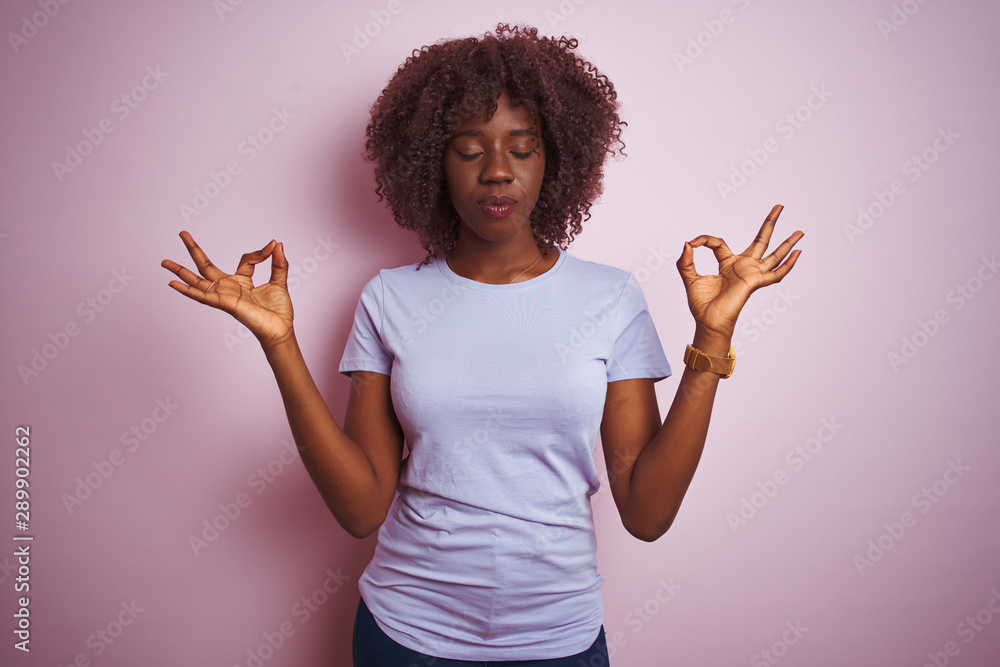 Young african afro woman wearing t-shirt standing over isolated pink background relax and smiling with eyes closed doing meditation gesture with fingers. Yoga concept. Young african afro woman wearing t-shirt standing over isolated pink background relax and smiling with eyes closed doing meditation gesture with fingers. Yoga concept.