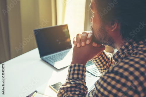 Serious businessman looking at laptop screen and thinking on problem while sitting in office.