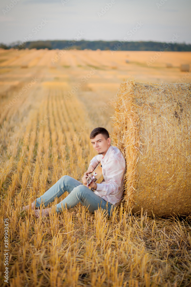 young guy is relaxing in the countryside with a guitar. Plays the guitar . Resting lying on the hay young guy is relaxing in the countryside with a guitar. Plays the guitar . Resting lying on the hay