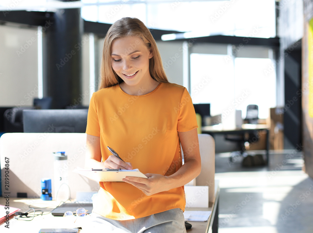 Beautiful business woman is smiling and writing something down while standing in the office