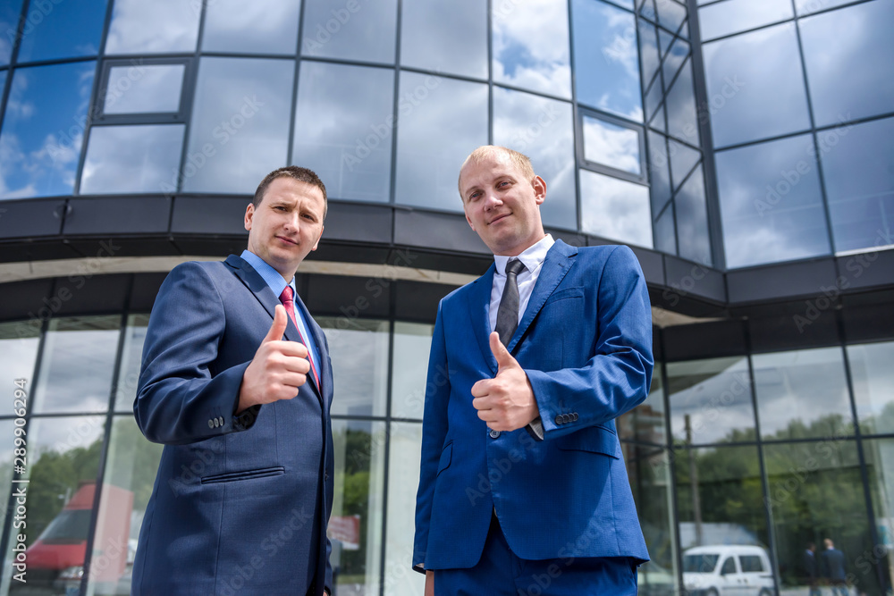 Two men in suits showing thumbs up outdoors Two men in suits showing thumbs up outdoors