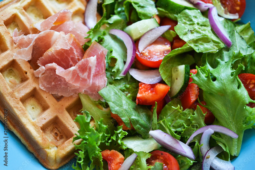Belgian waffles with prosciutto and vegetable salad on the kitchen table. Belgian waffles with prosciutto and vegetable salad on the kitchen table.