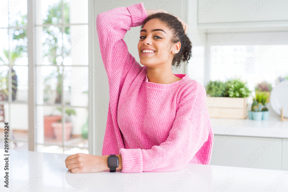 Beautiful african american woman with afro hair wearing casual pink sweater smiling confident touching hair with hand up gesture, posing attractive and fashionable Beautiful african american woman with afro hair wearing casual pink sweater smiling confident touching hair with hand up gesture, posing attractive and fashionable