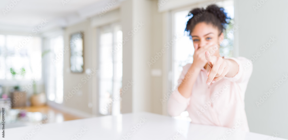 Wide angle of beautiful african american woman with afro hair laughing at you, pointing finger to the camera with hand over mouth, shame expression Wide angle of beautiful african american woman with afro hair laughing at you, pointing finger to the camera with hand over mouth, shame expression