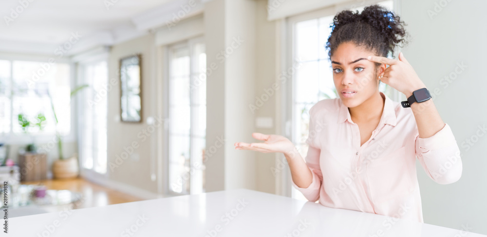 Wide angle of beautiful african american woman with afro hair confused and annoyed with open palm showing copy space and pointing finger to forehead. Think about it.