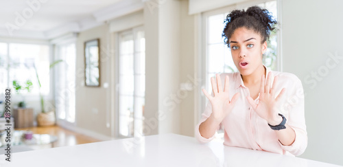 Wide angle of beautiful african american woman with afro hair Moving away hands palms showing refusal and denial with afraid and disgusting expression. Stop and forbidden.