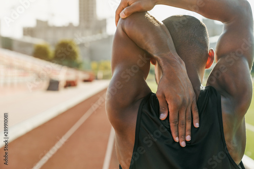 Photos Rear view of a man athlete doing stretching exercises in a track and field stadi