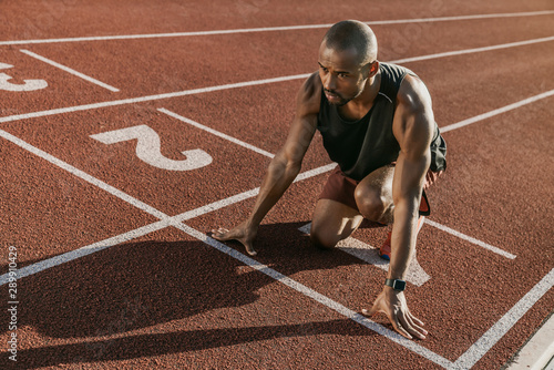 Young male athlete at starting block on running track preparing for run