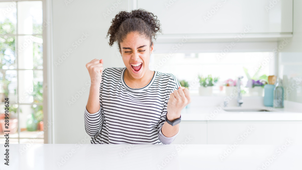 Beautiful african american woman with afro hair wearing casual striped sweater very happy and excited doing winner gesture with arms raised, smiling and screaming for success. Celebration concept. Beautiful african american woman with afro hair wearing casual striped sweater very happy and excited doing winner gesture with arms raised, smiling and screaming for success. Celebration concept.