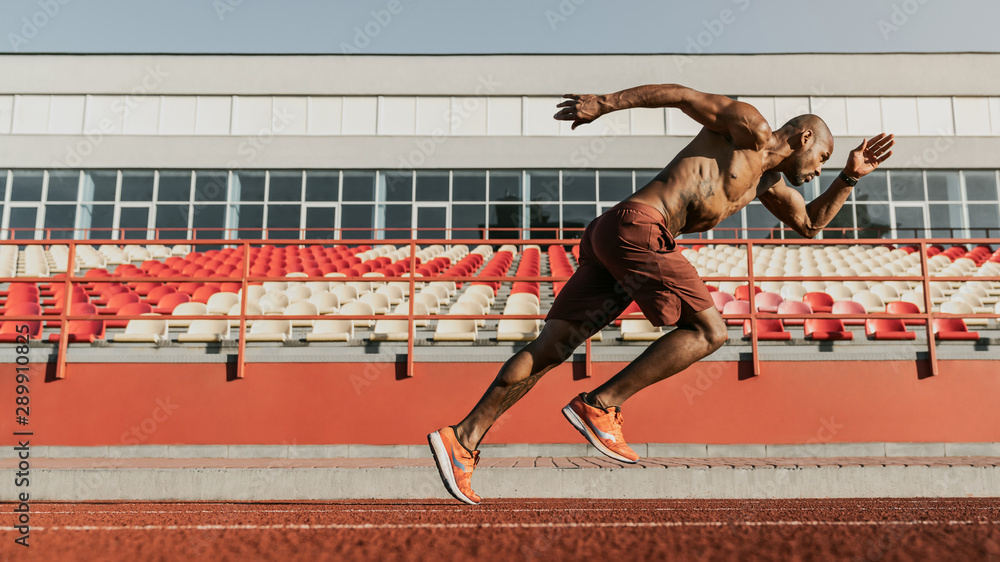 Side view shot of male sprinter running on the sport track. Athlete runner doing workout at the stadium фотография Stock