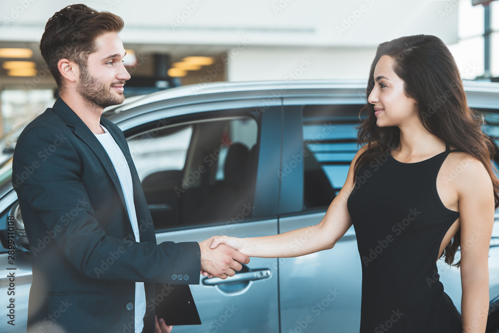 handsome man manager and beautiful brunette woman client shaking hands after succesful deal in dealership center handsome man manager and beautiful brunette woman client shaking hands after succesful deal in dealership center