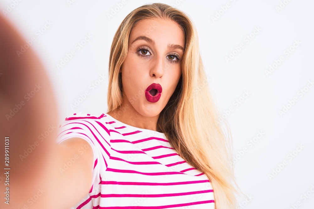 Beautiful woman wearing striped t-shirt make selfie by camera over isolated white background scared in shock with a surprise face, afraid and excited with fear expression Beautiful woman wearing striped t-shirt make selfie by camera over isolated white background scared in shock with a surprise face, afraid and excited with fear expression
