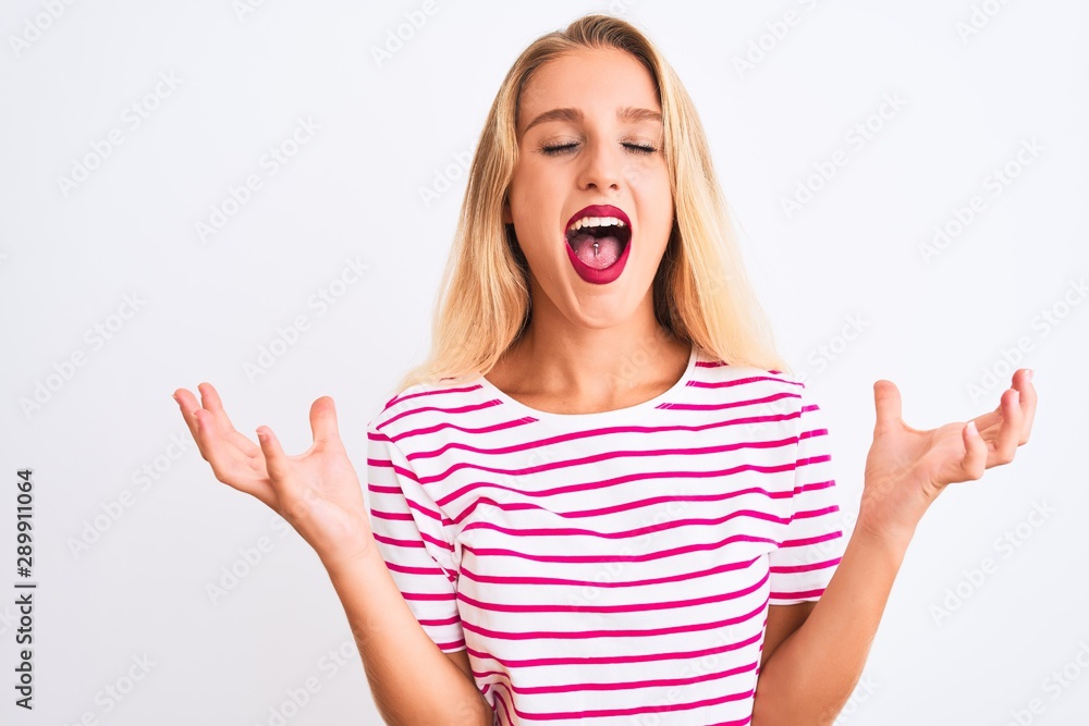 Young beautiful woman wearing pink striped t-shirt standing over isolated white background celebrating mad and crazy for success with arms raised and closed eyes screaming excited. Winner concept Young beautiful woman wearing pink striped t-shirt standing over isolated white background celebrating mad and crazy for success with arms raised and closed eyes screaming excited. Winner concept