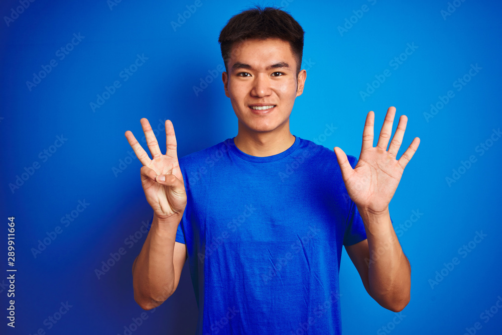Young asian chinese man wearing t-shirt standing over isolated blue background showing and pointing up with fingers number eight while smiling confident and happy. Young asian chinese man wearing t-shirt standing over isolated blue background showing and pointing up with fingers number eight while smiling confident and happy.