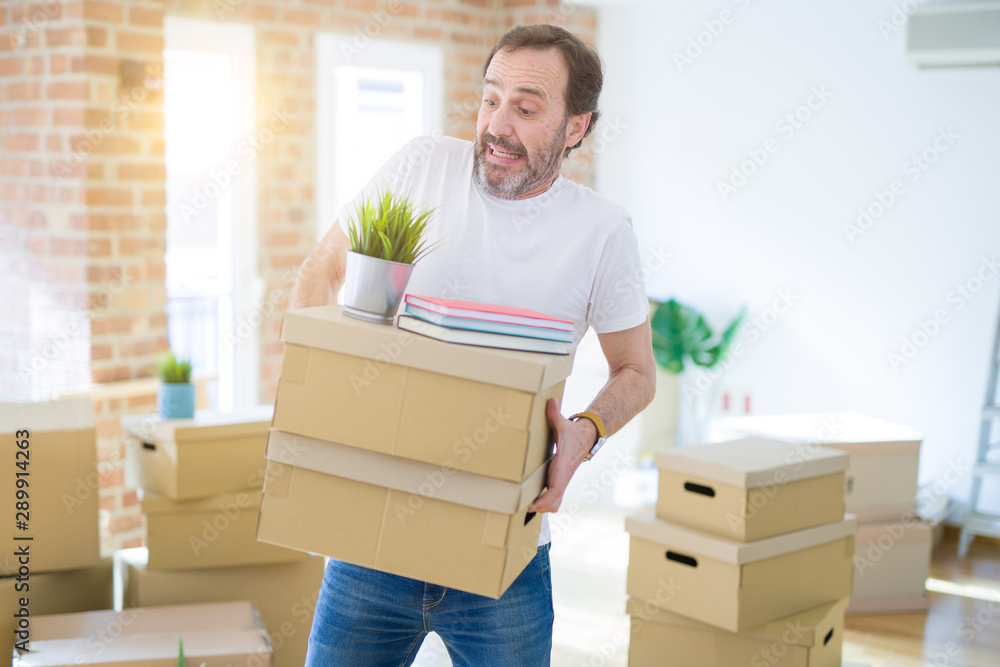 Handsome middle age senior nervous man triying to hold cardboard boxes, upset for box falling Handsome middle age senior nervous man triying to hold cardboard boxes, upset for box falling