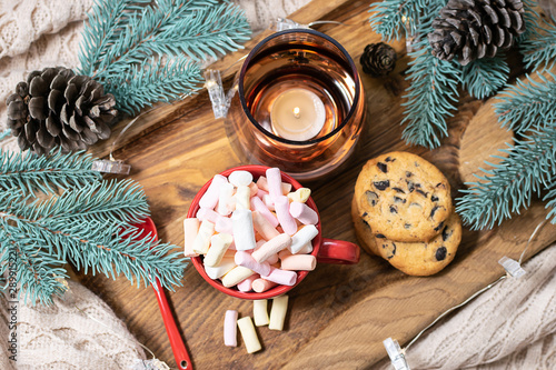 Cozy Christmas composition with cup of hot chocolate with marshmallows, homemade cookies, warm blanket and candles. Hygge winter interior. New year and Christmas concept. photo