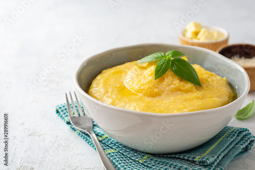 Polenta with butter and parmesan cheese in bowl on concrete background. Selective focus.