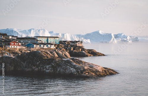 Aerial View of Arctic city of Ilulissat, Greenland during sunrise sunset with fog. Colorful houses in the center of the town with icebergs in the background in summer on a sunny day with orange pink photo