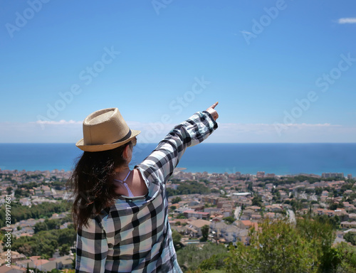 Attractive tourist in a hat shows a hand in front of him to the sky, standing on a hill