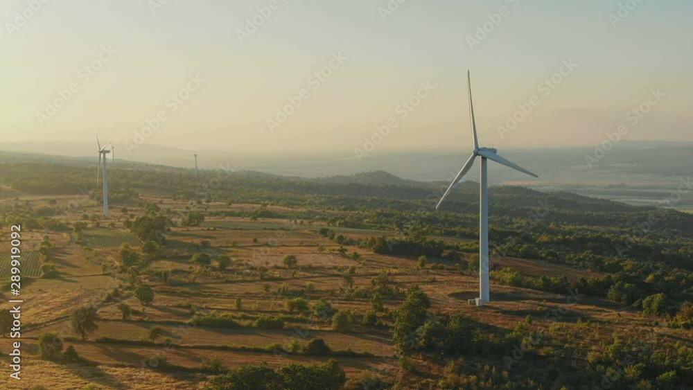 Flying to the Wind turbines generating renewable and sustainable energy in the mountains. Morning sunrise light, Aerial view from Drone, rural countryside scene and green forest background Flying to the Wind turbines generating renewable and sustainable energy in the mountains. Morning sunrise light, Aerial view from Drone, rural countryside scene and green forest background