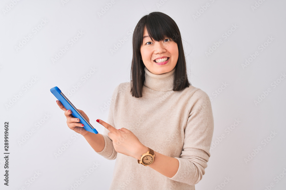 Beautiful chinese woman using blue tablet standing over isolated white background very happy pointing with hand and finger Beautiful chinese woman using blue tablet standing over isolated white background very happy pointing with hand and finger