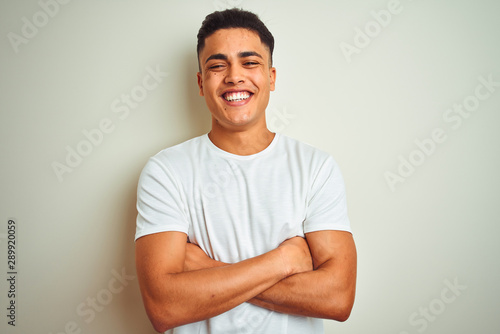 Young brazilian man wearing t-shirt standing over isolated white background happy face smiling with crossed arms looking at the camera. Positive person.