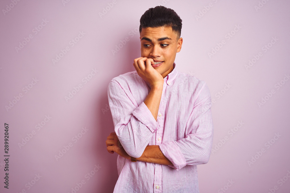 Young brazilian man wearing shirt standing over isolated pink background looking stressed and nervous with hands on mouth biting nails. Anxiety problem. Young brazilian man wearing shirt standing over isolated pink background looking stressed and nervous with hands on mouth biting nails. Anxiety problem.