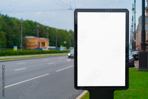 White vertical billboard on the lawn near the road with white mockup background. standing in the city
