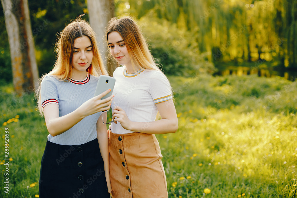 two beautiful young beautiful girls with shiny blond hair and a skirt and walk and spend goood time in a sunny summer park