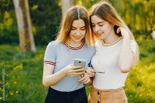 two beautiful young beautiful girls with shiny blond hair and a skirt and walk and spend goood time in a sunny summer park photo