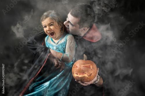 Halloween portrait, vampire attacking young princess, man holding small pumpkin smoke background