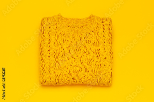 Autumn flat lay composition. Orange yellow knitted woolen female sweater on yellow background top view copy space. Fashionable women's fall winter accessories. Cozy Knit Jumper Stylish Lady Clothes