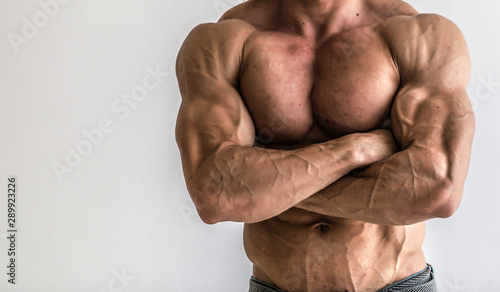 Bodybuilder flexing his muscles in studio. The torso of attractive male body builder on white background.