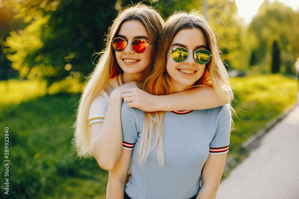Fototapeta premium two beautiful young beautiful girls with shiny blond hair and a skirt and walk and spend goood time in a sunny summer park