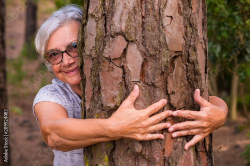 A pair of human hands hugging a tree in the woods - love for the outdoors and nature - earth day concept. An old woman hiding from the trunk. People save the planet from deforestation