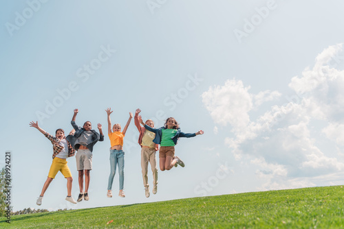 happy multicultural kids jumping and gesturing against blue sky