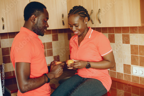 a beautiful young black girl in a pink T-shirt and blue jeans standing at home in the kitchen with her boyfriend and eating the apple